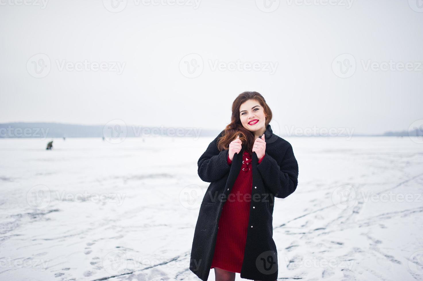 modelo morena de talla grande en rojo contra el lago congelado en el día de invierno. foto