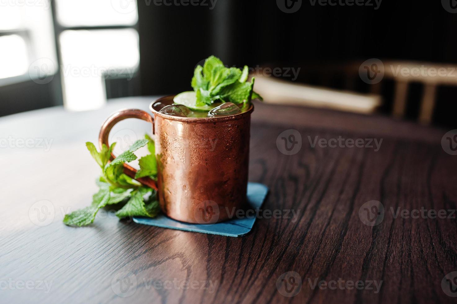 Alcoholic cocktail with ice, mint and lime in bronze cup on bar table. photo