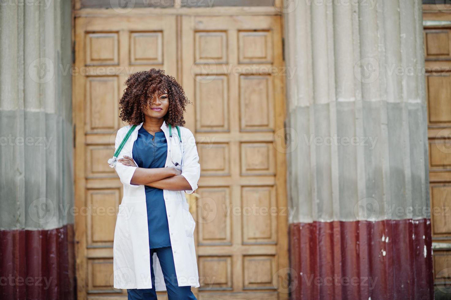 African american doctor female at lab coat with stethoscope outdoor against clinic door. photo