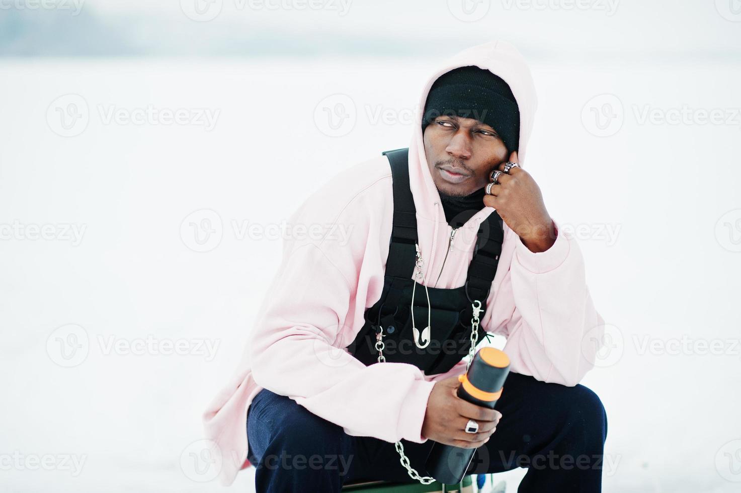 African american fisherman with thermos sitting on frozen lake. Winter fishing. photo