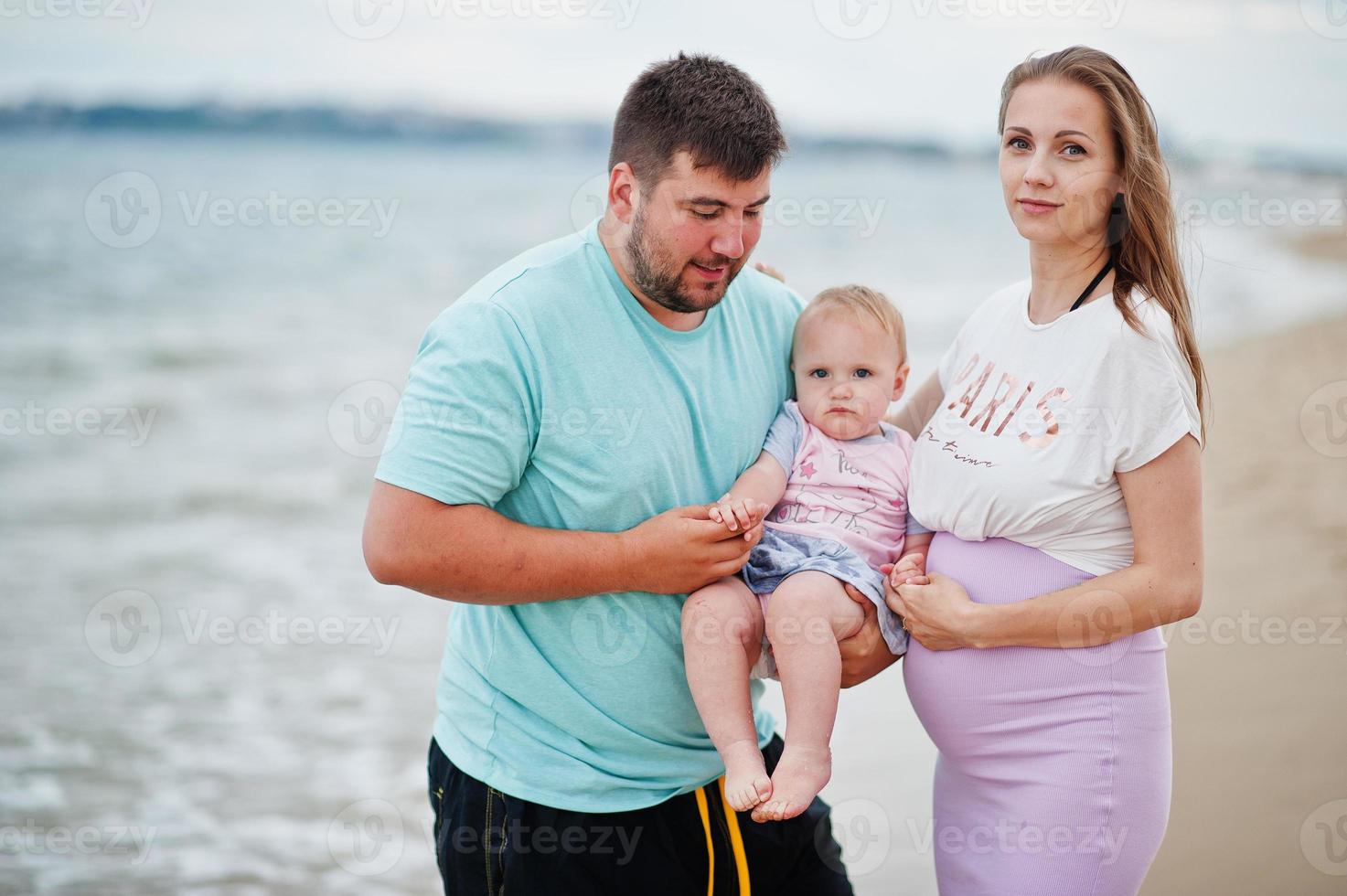 Summer vacations. Parents and people outdoor activity with children. Happy family holidays. Father, pregnant mother, baby daughter on sea sand beach. photo