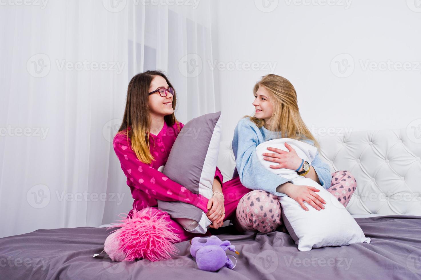 Two friends girls in pajamas having fun on bed at room. photo