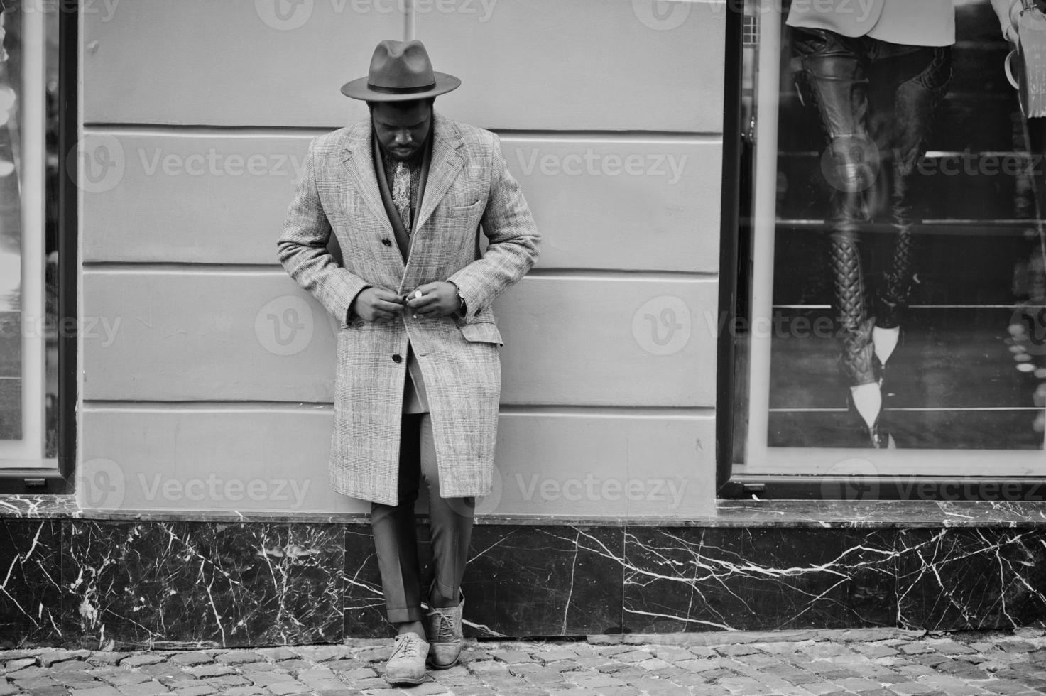 elegante modelo afroamericano con abrigo gris, corbata de chaqueta y sombrero rojo. foto en blanco y negro.