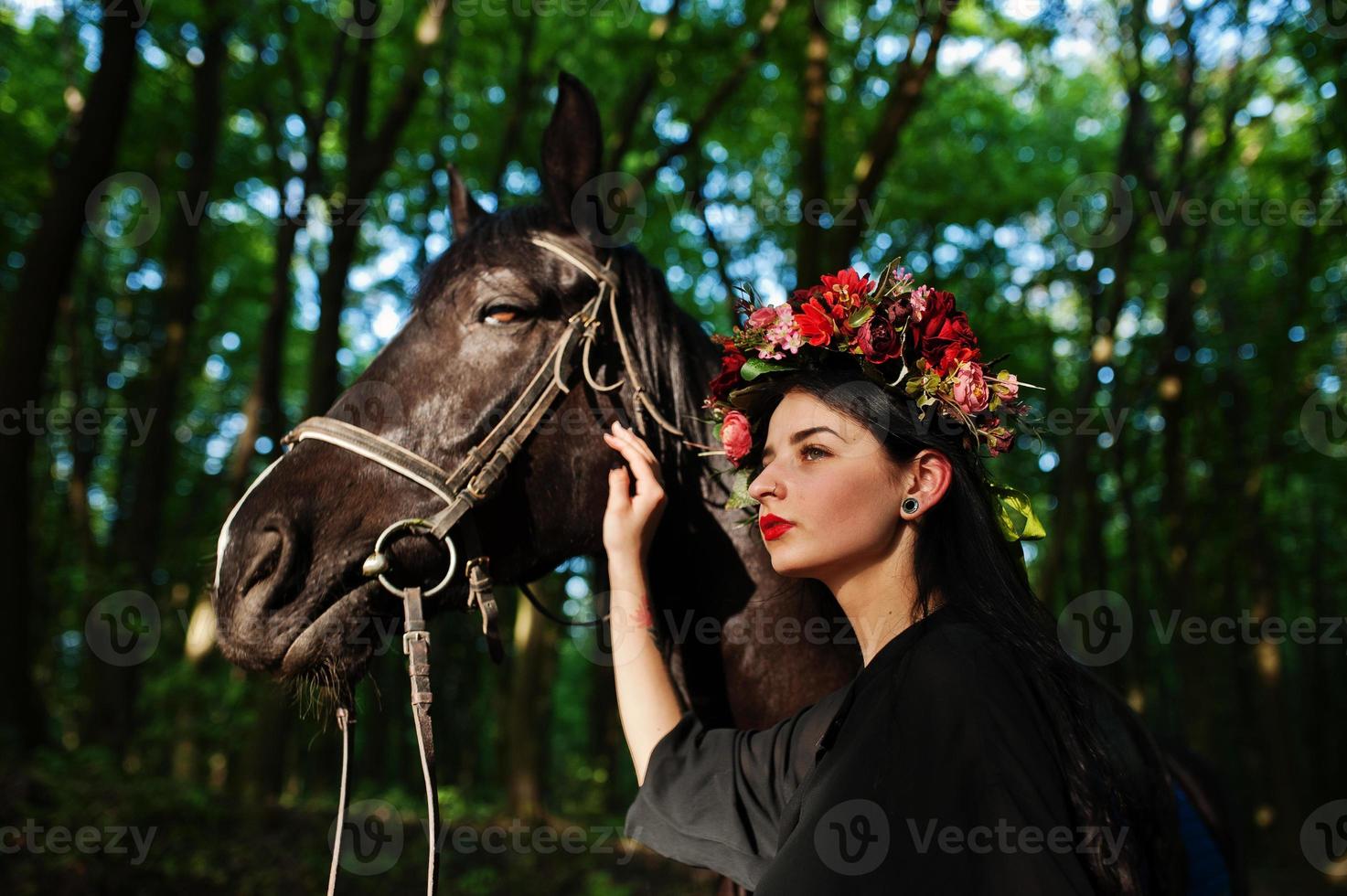 Mystical girl in wreath wear in black with horse in wood. photo