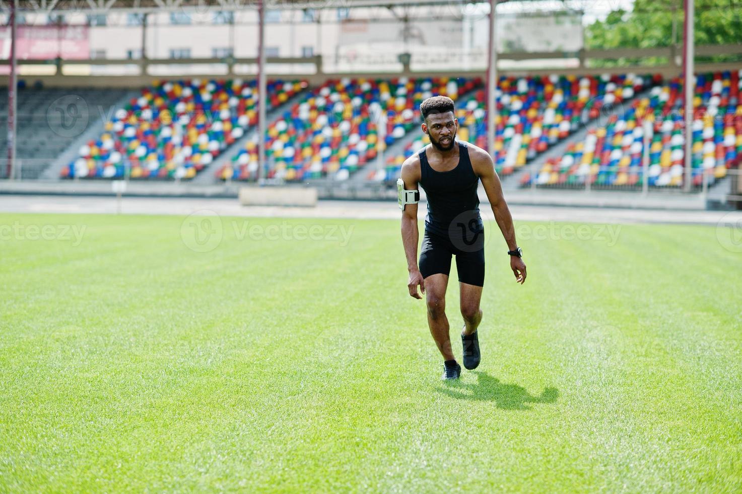 African american male athlete in sportswear doing jump exercise at stadium. photo
