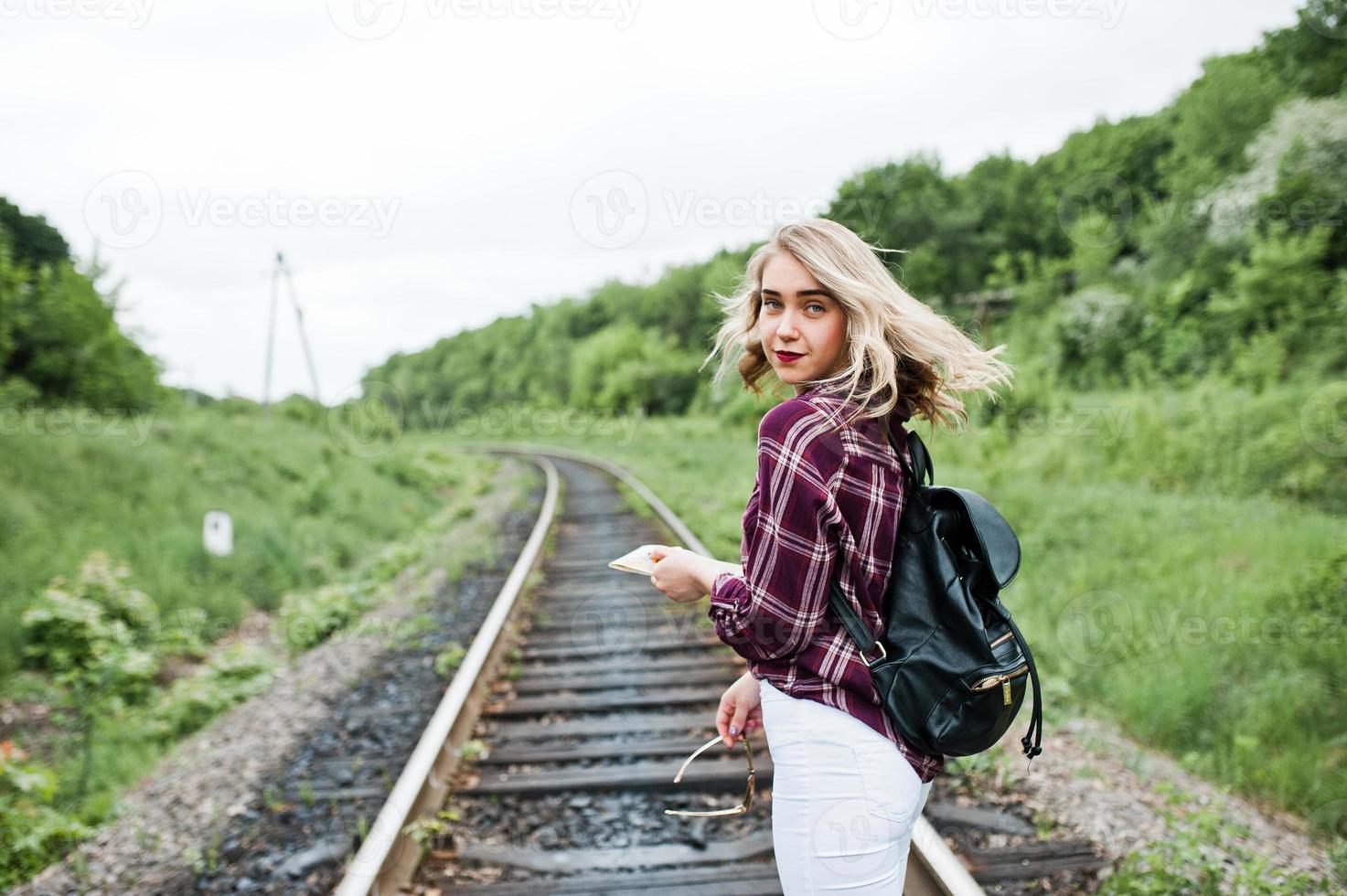 Portrait of a pretty blond girl in tartan shirt walking on the railway with map in her hands. photo