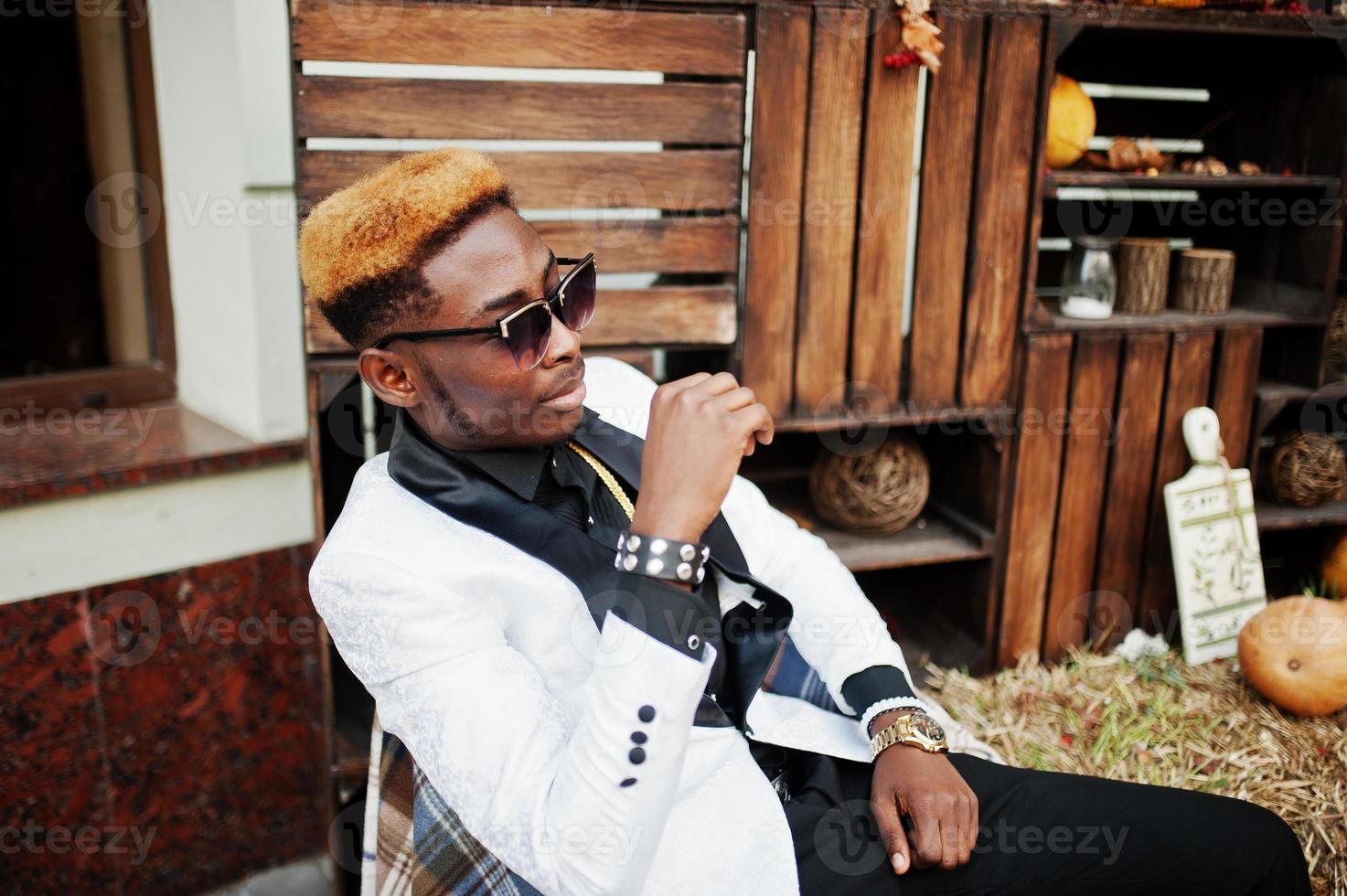 hombre afroamericano elegante y guapo con traje blanco sentado en una silla. foto