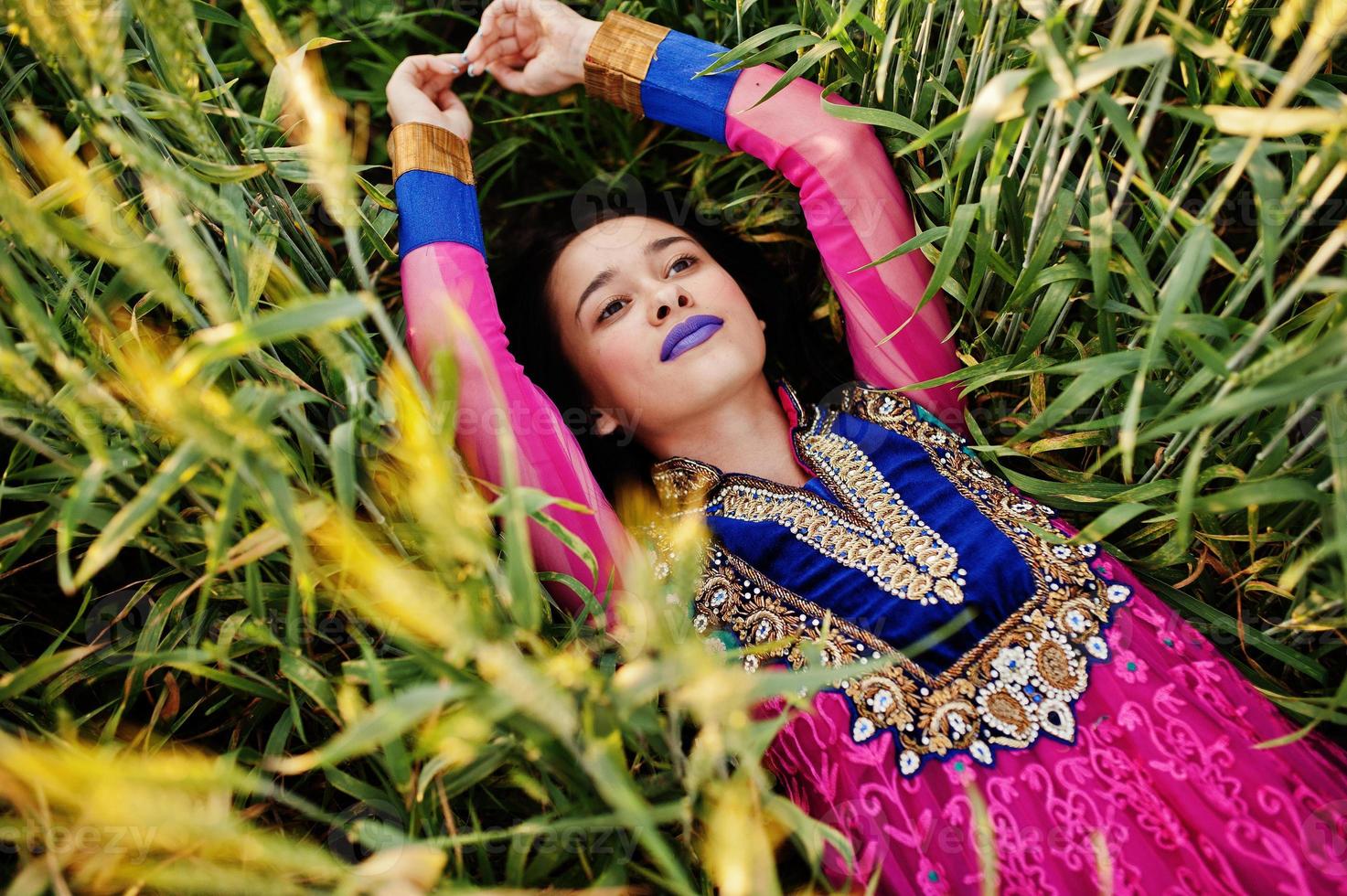 tierna niña india en sari, con maquillaje de labios violetas posada en el campo al atardecer. modelo indio de moda. foto