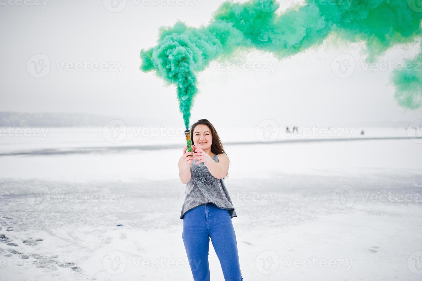 Young girl with green colored smoke bomb in hand in winter day. photo