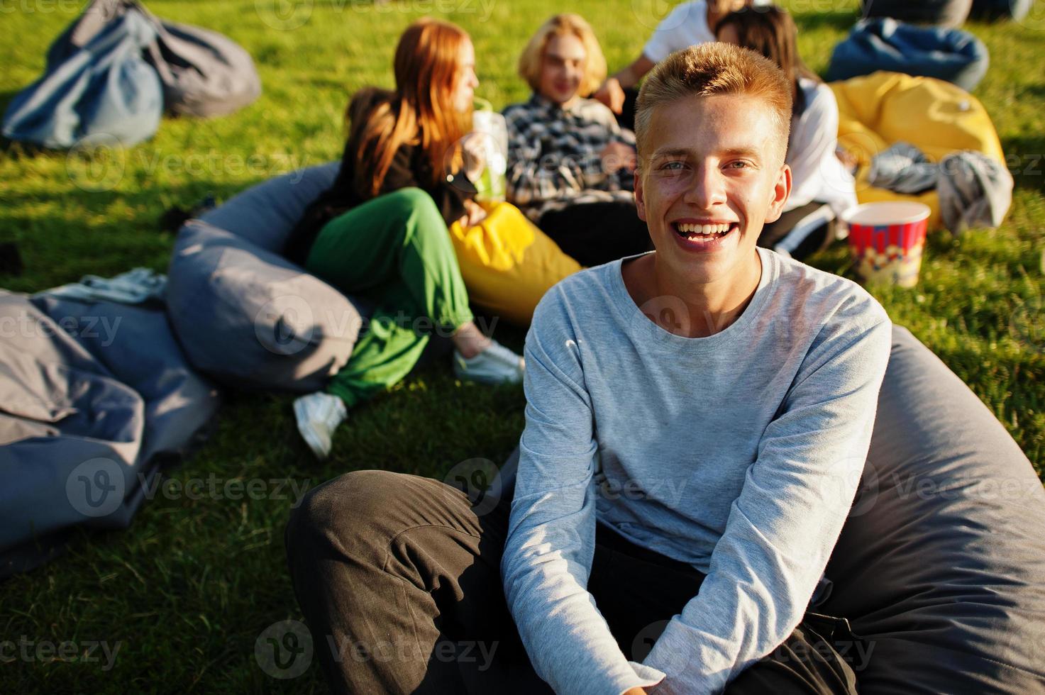 Young multi ethnic group of people watching movie at poof in open air cinema. Close up portrait of funny guy. photo