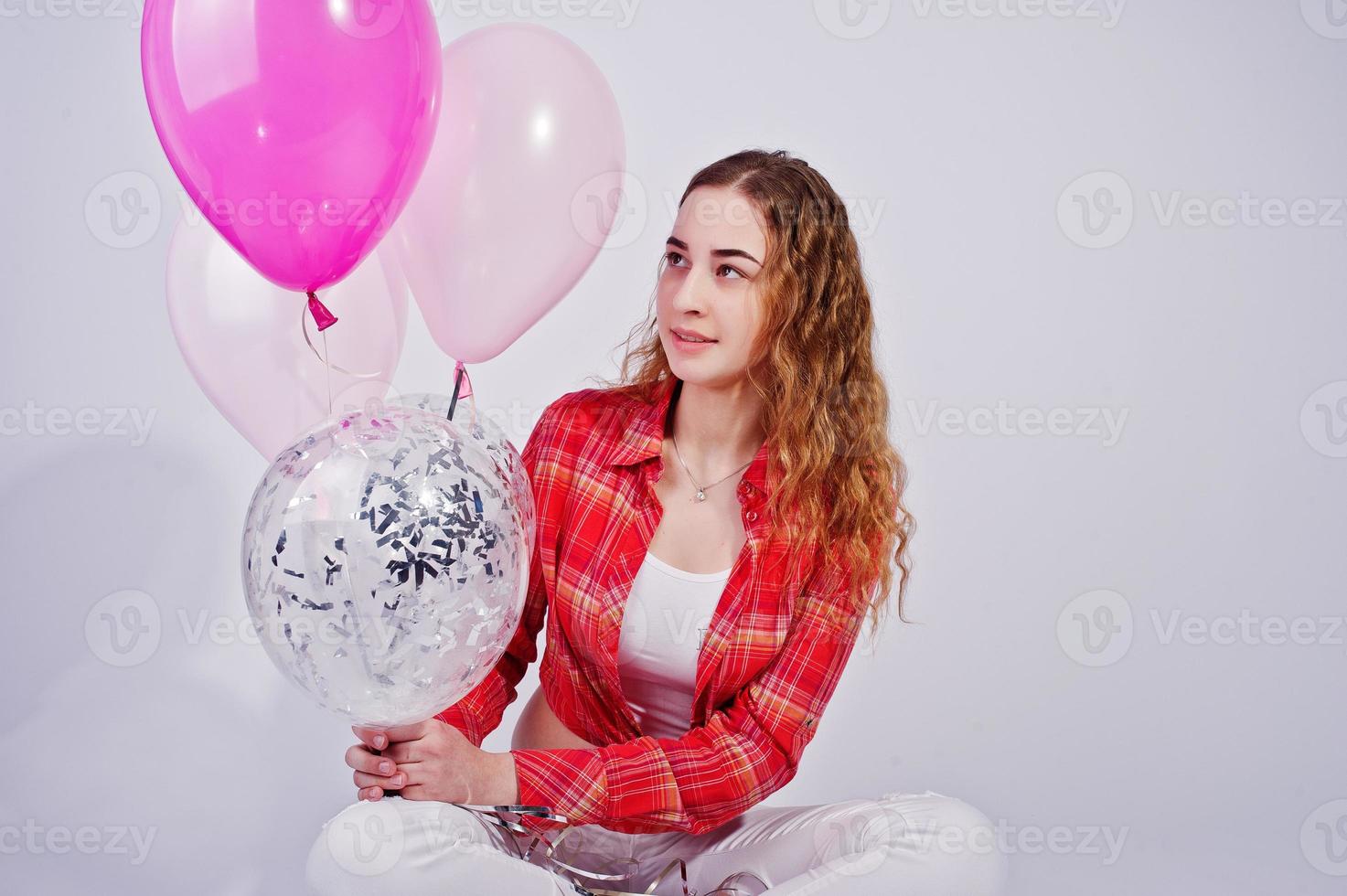 Young girl in red checked shirt and white pants with balloons against white background on studio. photo