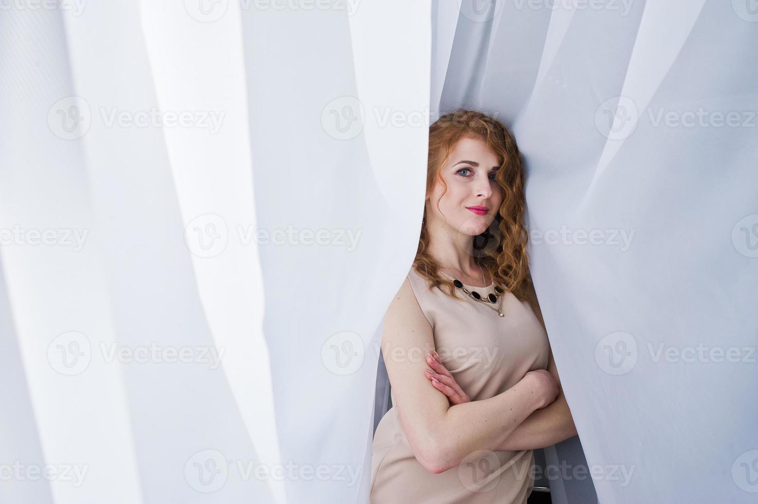 Curly hair girl on beige dress posed at white curtains. photo