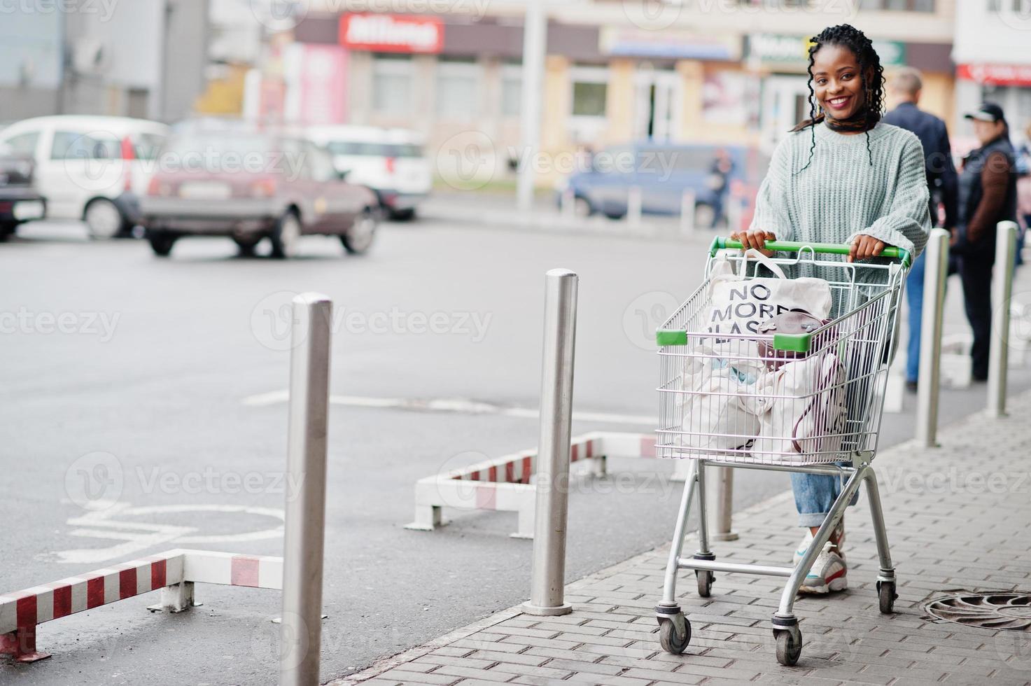 mujer africana con carrito de compras posó en el mercado al aire libre cerca del estacionamiento. foto