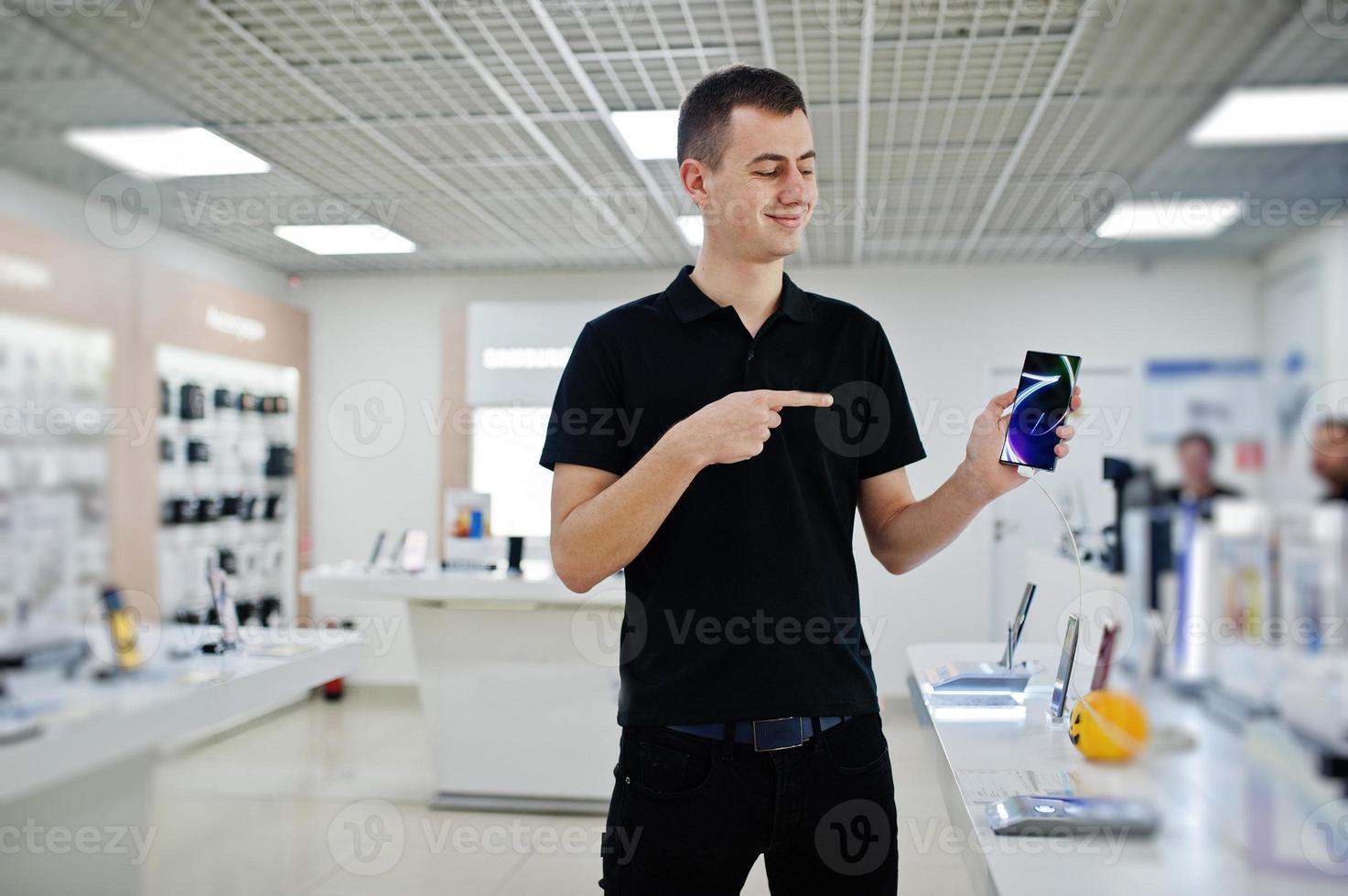 Seller man mobile phone professional consultant in tech store or shop hold new smartphone at  hand and show finger to the screen. photo