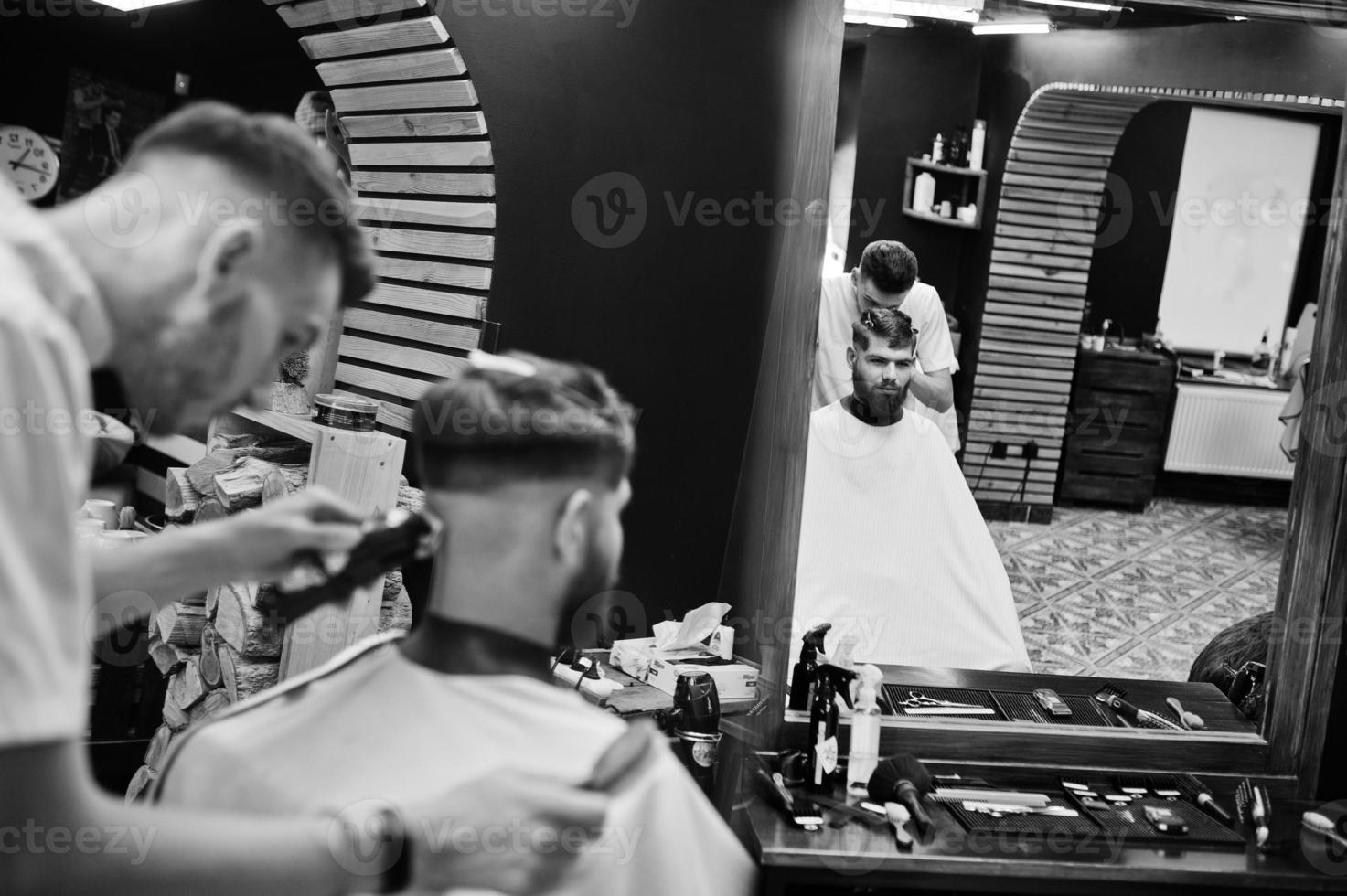 un joven barbudo que se corta el pelo con un peluquero mientras se sienta en una silla en la barbería. alma de barbero. foto