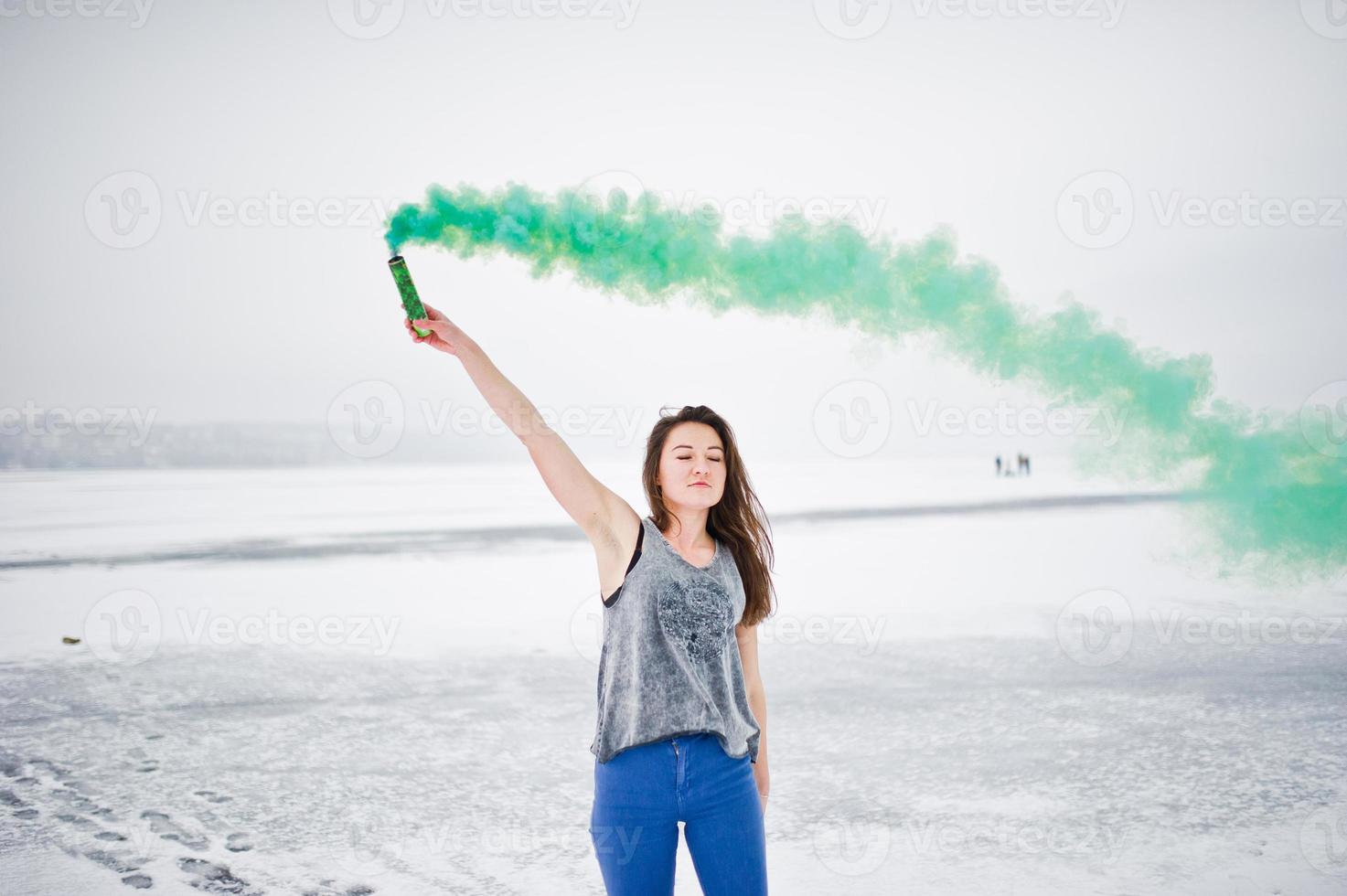 Young girl with green colored smoke bomb in hand in winter day. photo