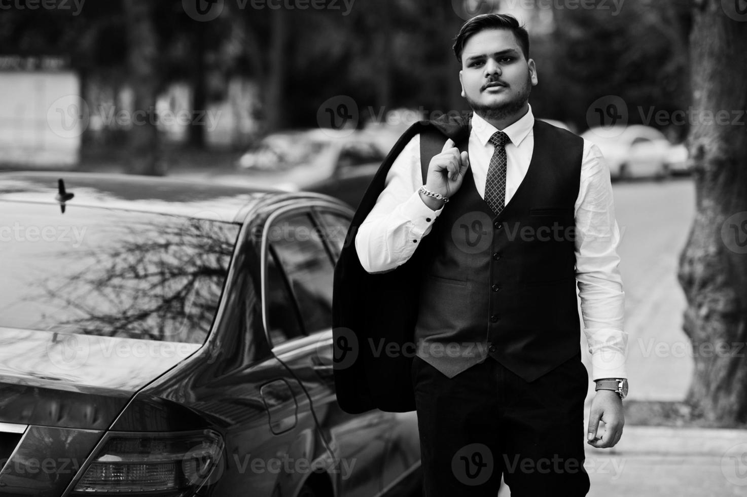 Stylish indian businessman in formal wear standing against black business car on street of city. photo