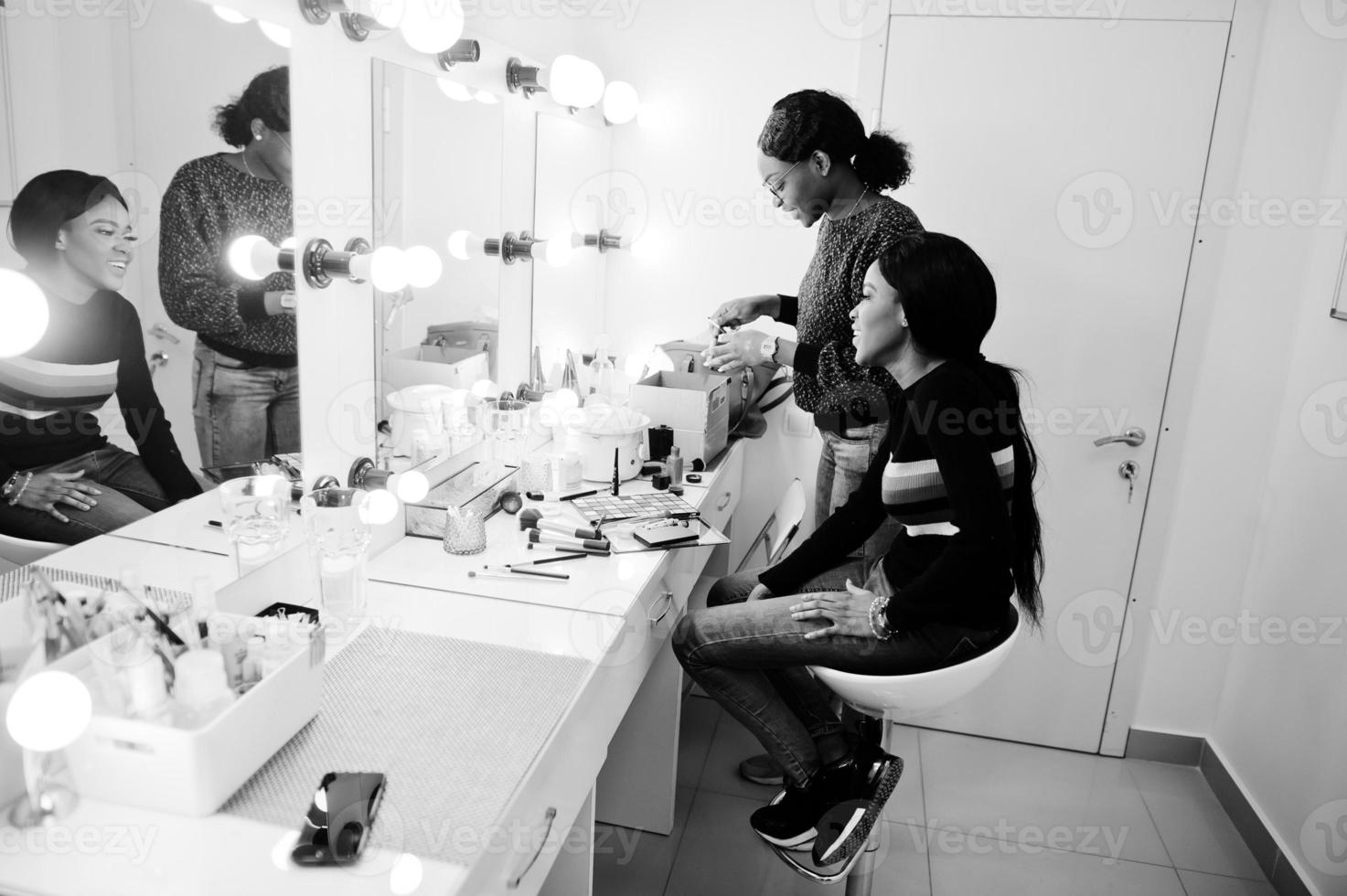 African American woman applying make-up by make-up artist at beauty saloon. photo