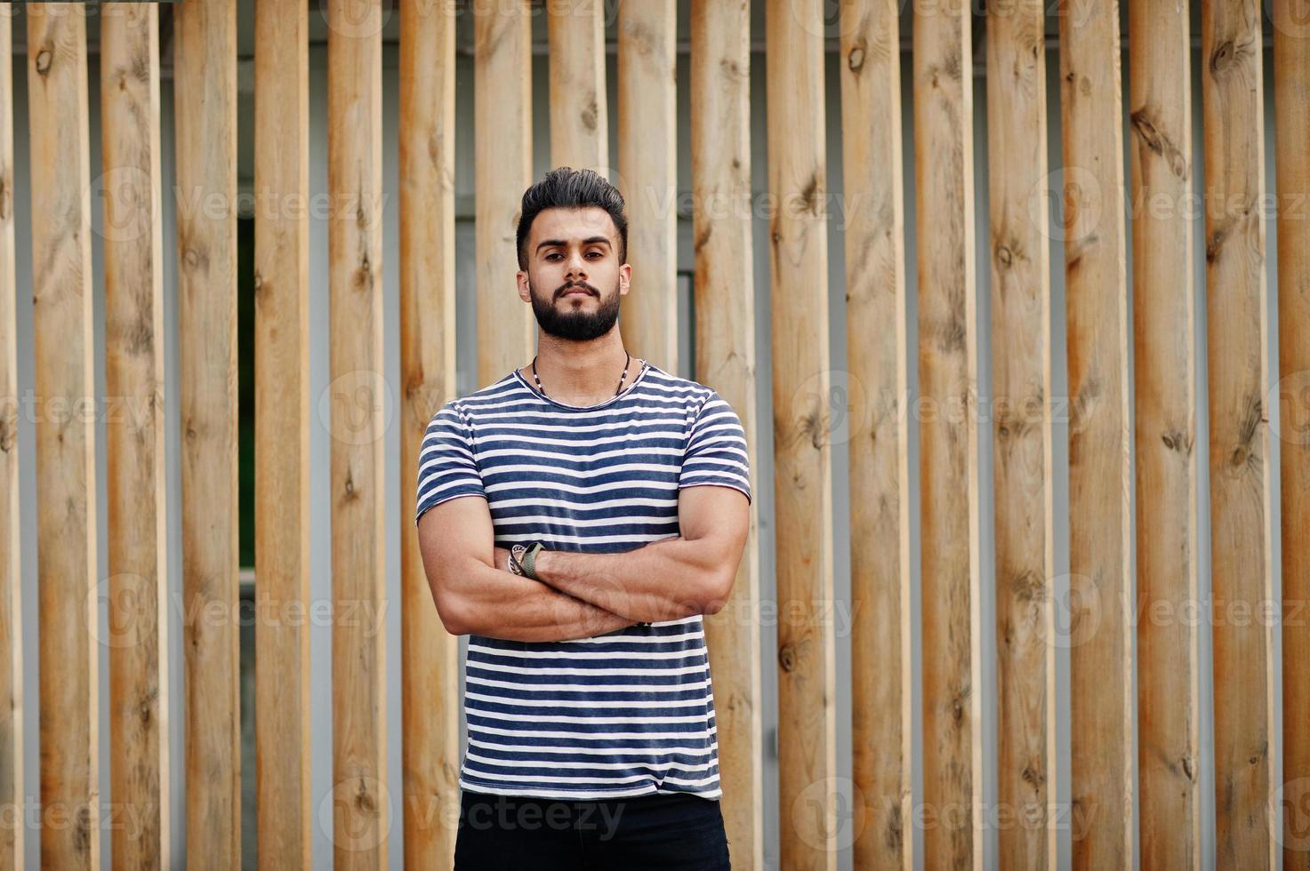 Handsome tall arabian beard man model at stripped shirt posed outdoor against wooden background. Fashionable arab guy. photo