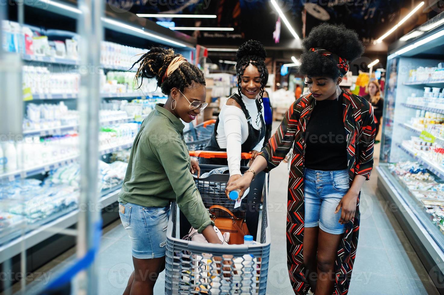 grupo de mujeres africanas con carritos de compras cerca del estante del refrigerador que venden productos lácteos hechos con leche en el supermercado. foto