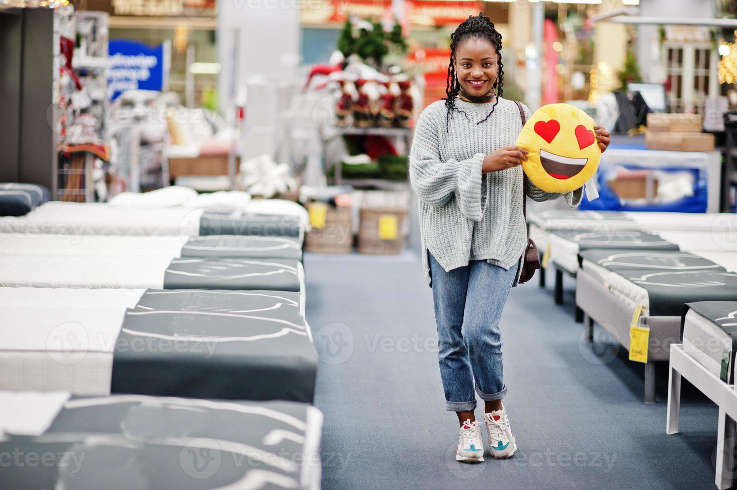 cara amor corazón emoji. mujer africana con almohada en una moderna tienda de muebles para el hogar. foto