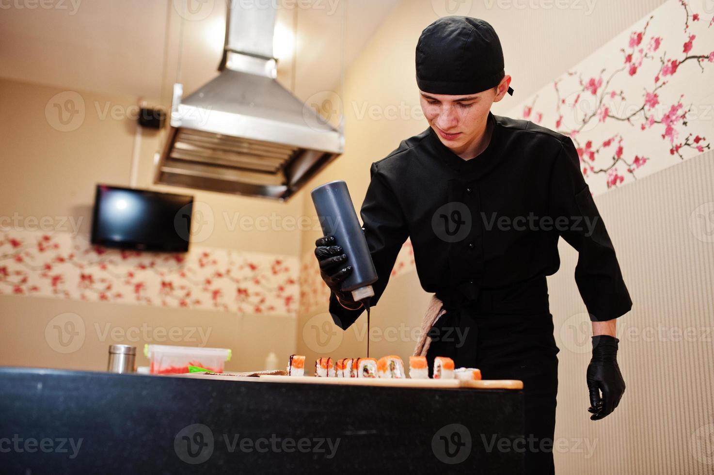 chef profesional vestido de negro haciendo sushi y rollos en la cocina de un restaurante de comida tradicional japonesa. foto