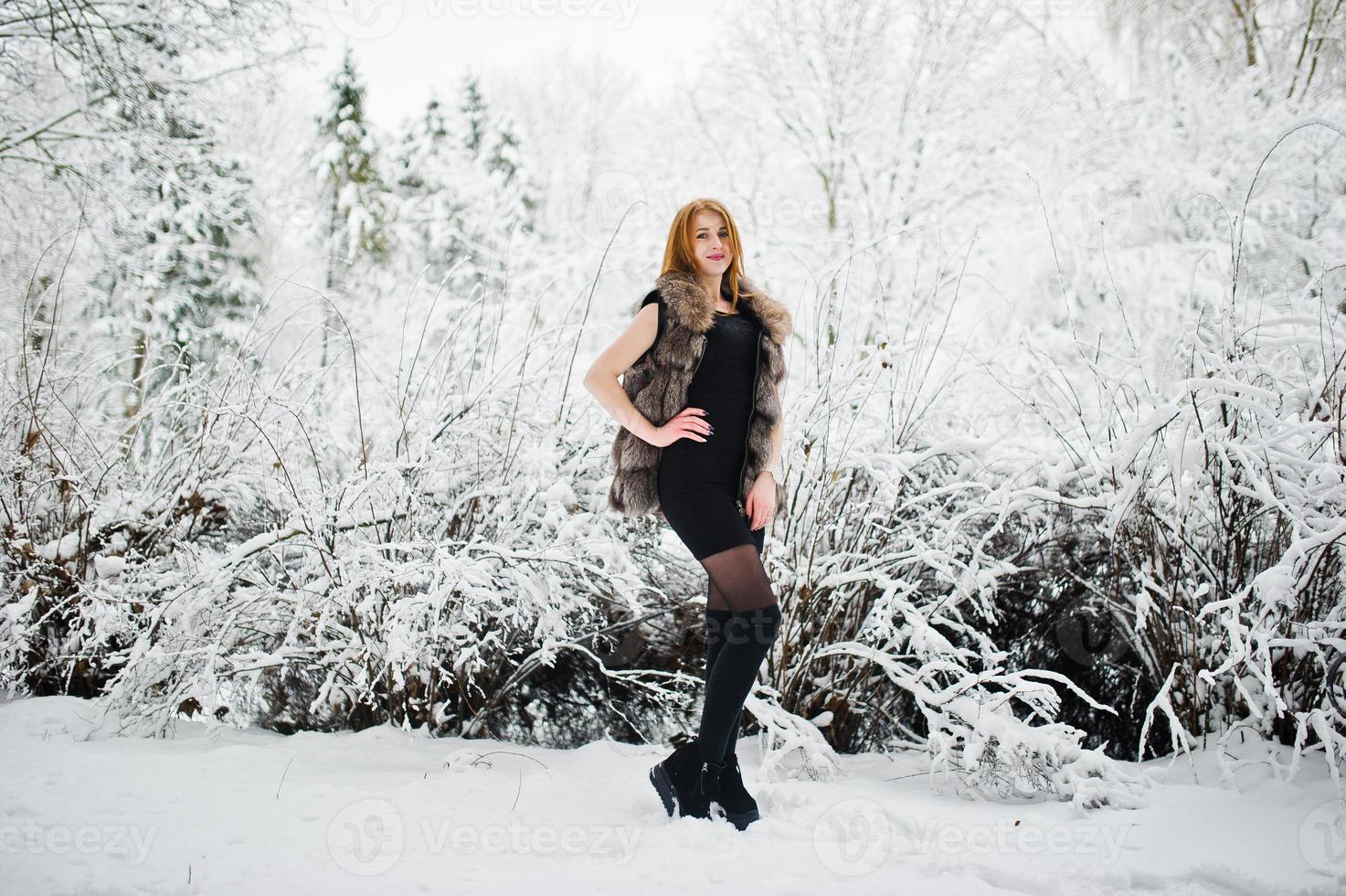 Red haired girl in fur coat walking at winter snowy park. photo