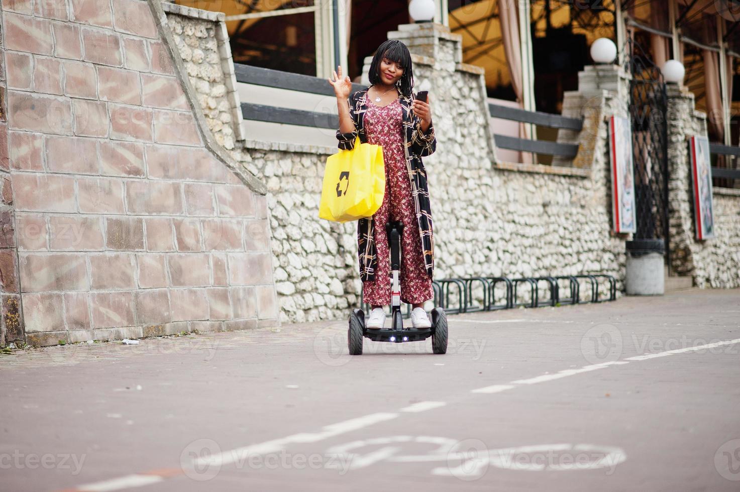 Beautiful african american woman using segway or hoverboard. Black girl with yellow  cloth eco bags recycling symbol. photo