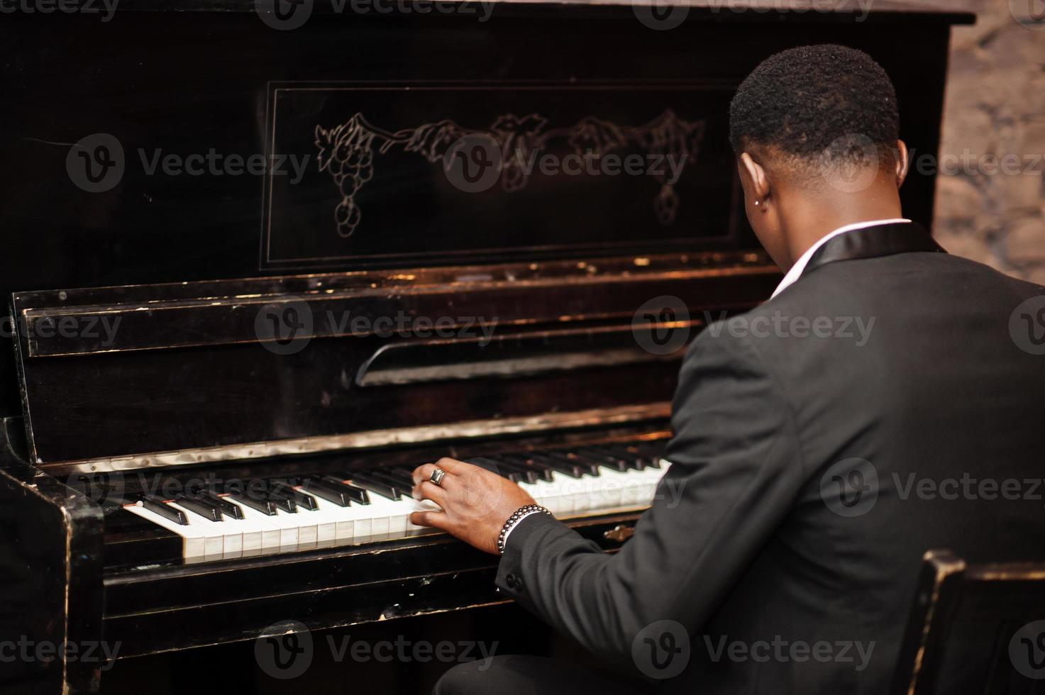 Back of strong powerful african american man in black suit play piano. photo