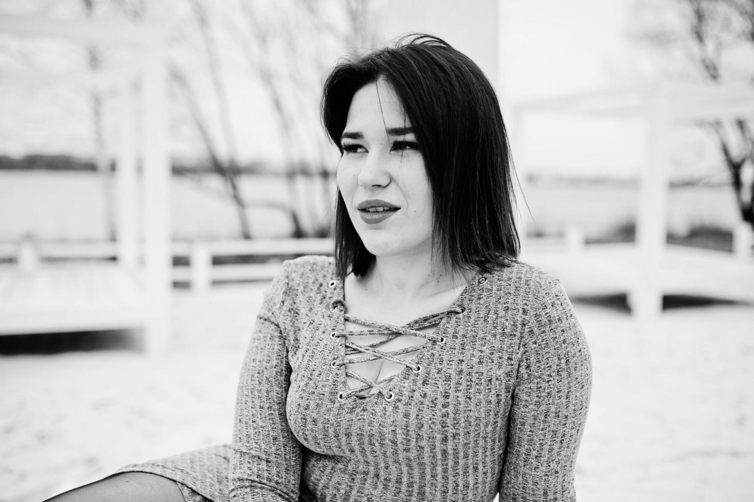 Portrait of brunette girl in gray dress sitting at white wooden construction. photo