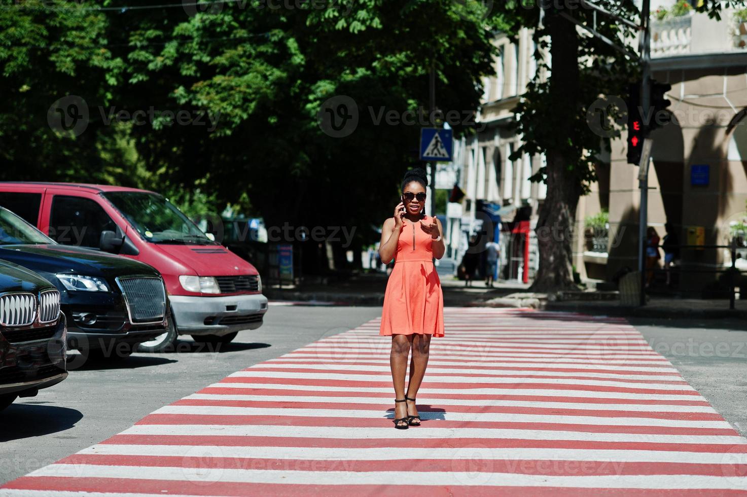 elegante mujer afroamericana caminando en el cruce de peatones o en el paso de peatones y hablando por teléfono móvil. foto