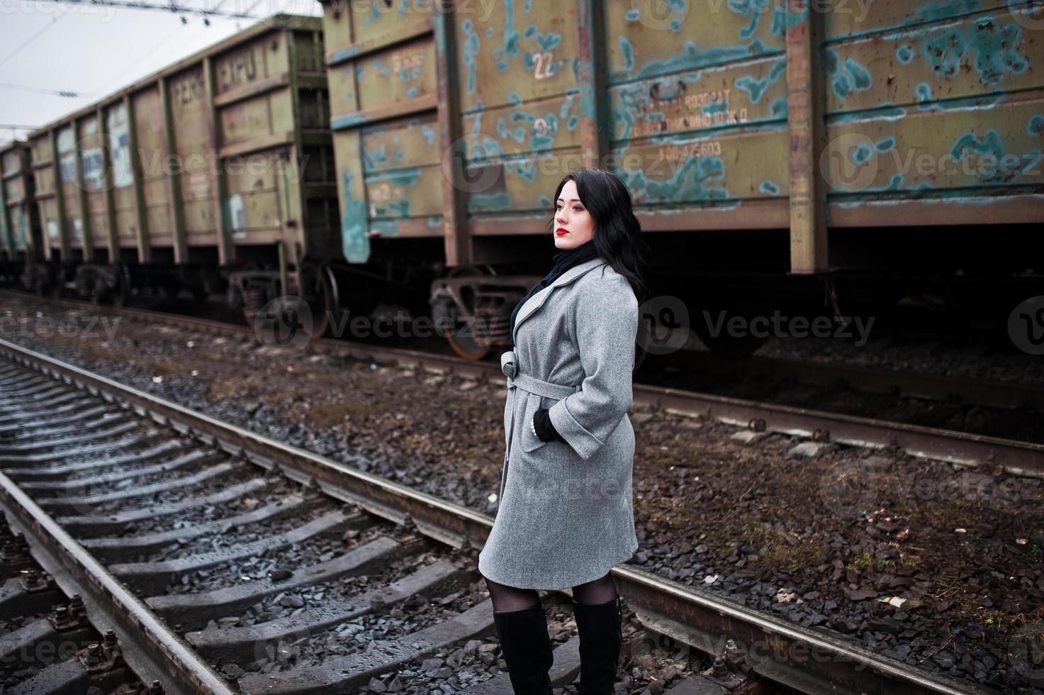 chica morena con abrigo gris posada en la estación de tren. foto