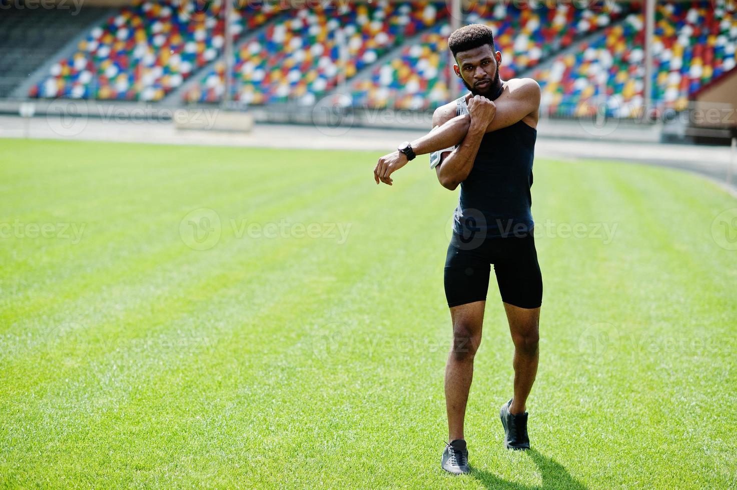 African american male athlete in sportswear doing stretching exercise at stadium. photo