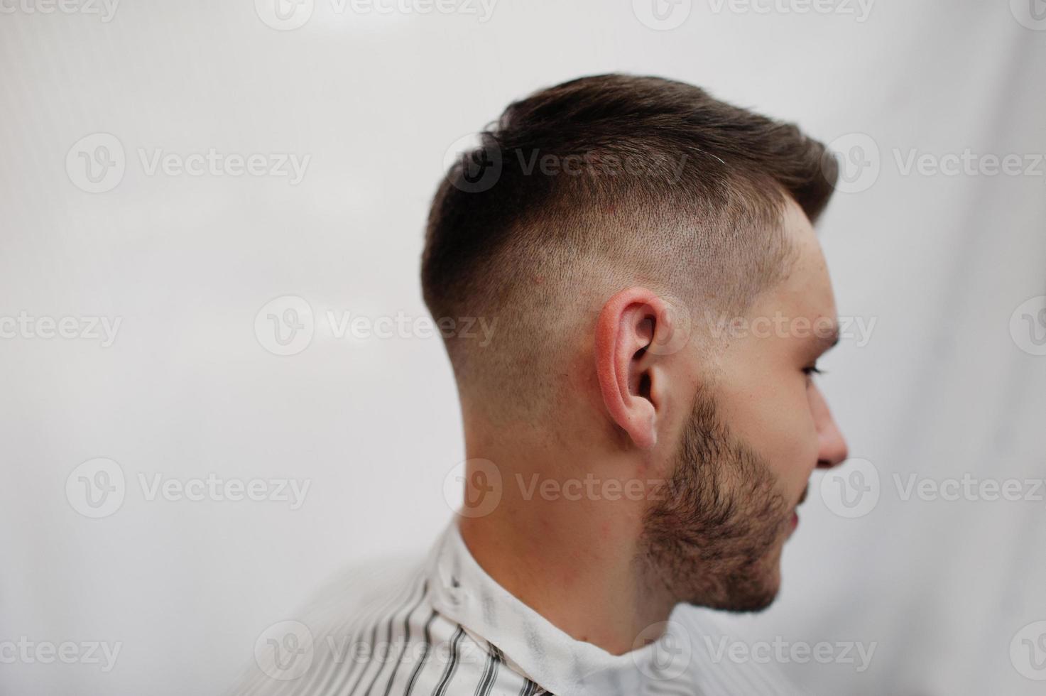 Close up head of young bearded man getting haircut at barbershop. Barber soul. photo