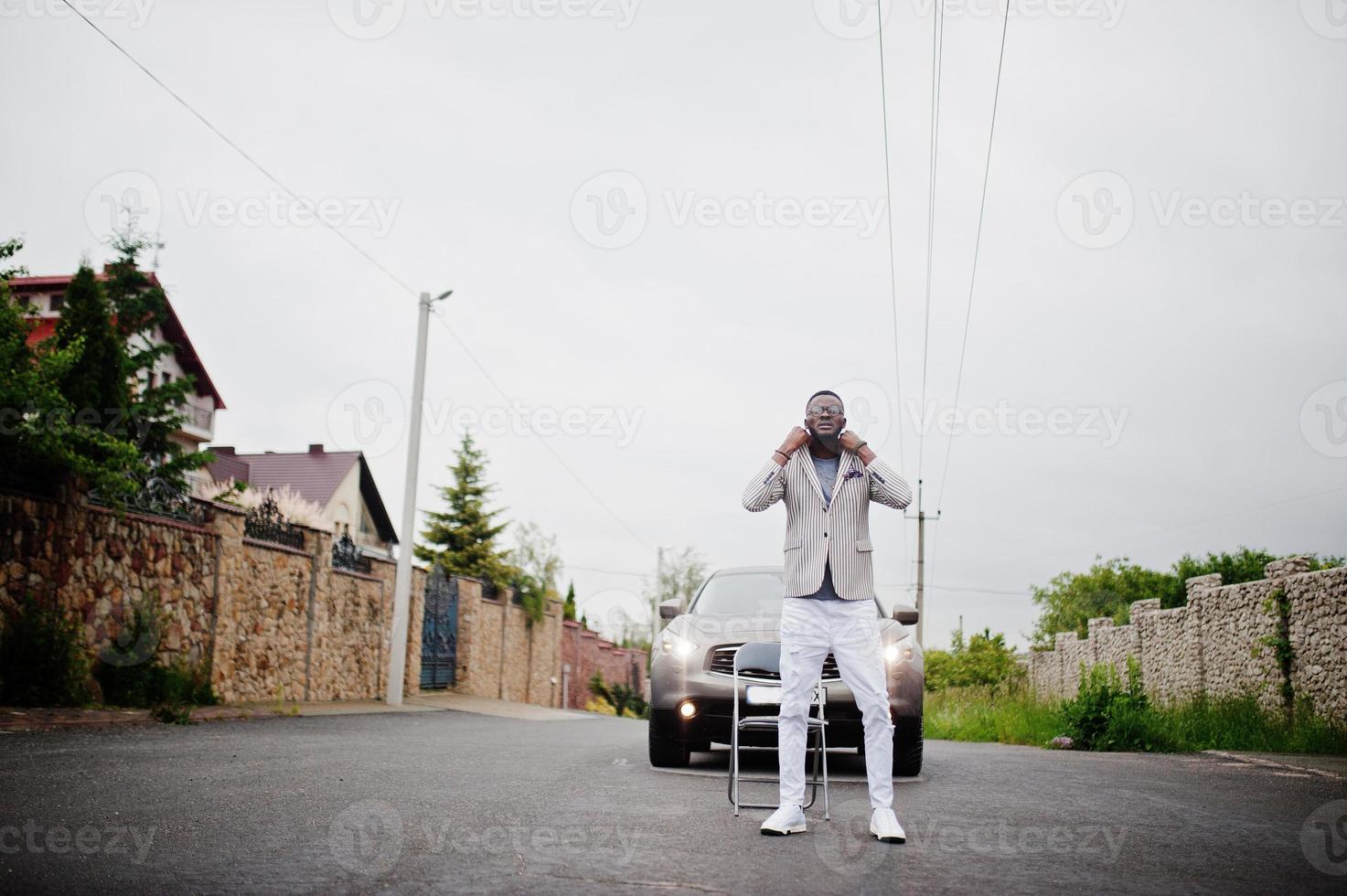 Rich and stylish african american man in blazer and white pants, eyeglasses posed against suv car. photo