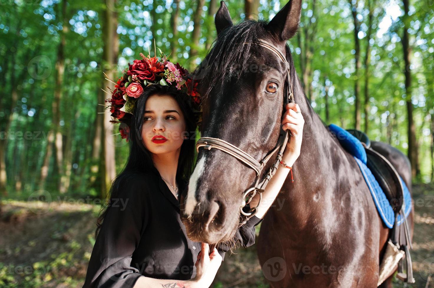 Mystical girl in wreath wear in black with horse in wood. photo