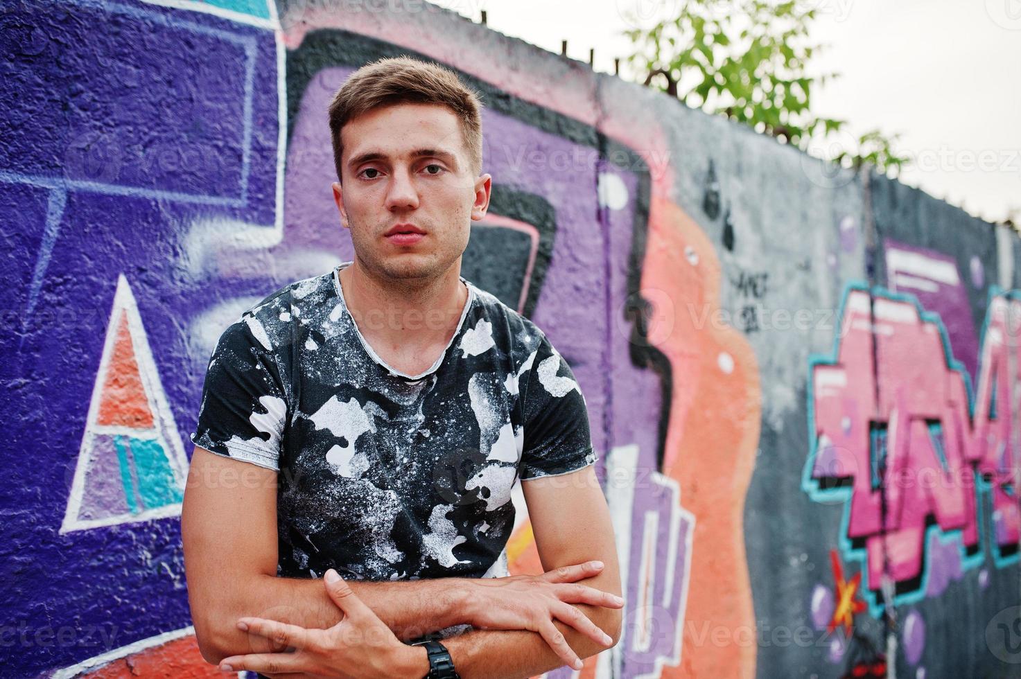 Lifestyle portrait of handsome man posing on the street of city with graffiti wall. photo