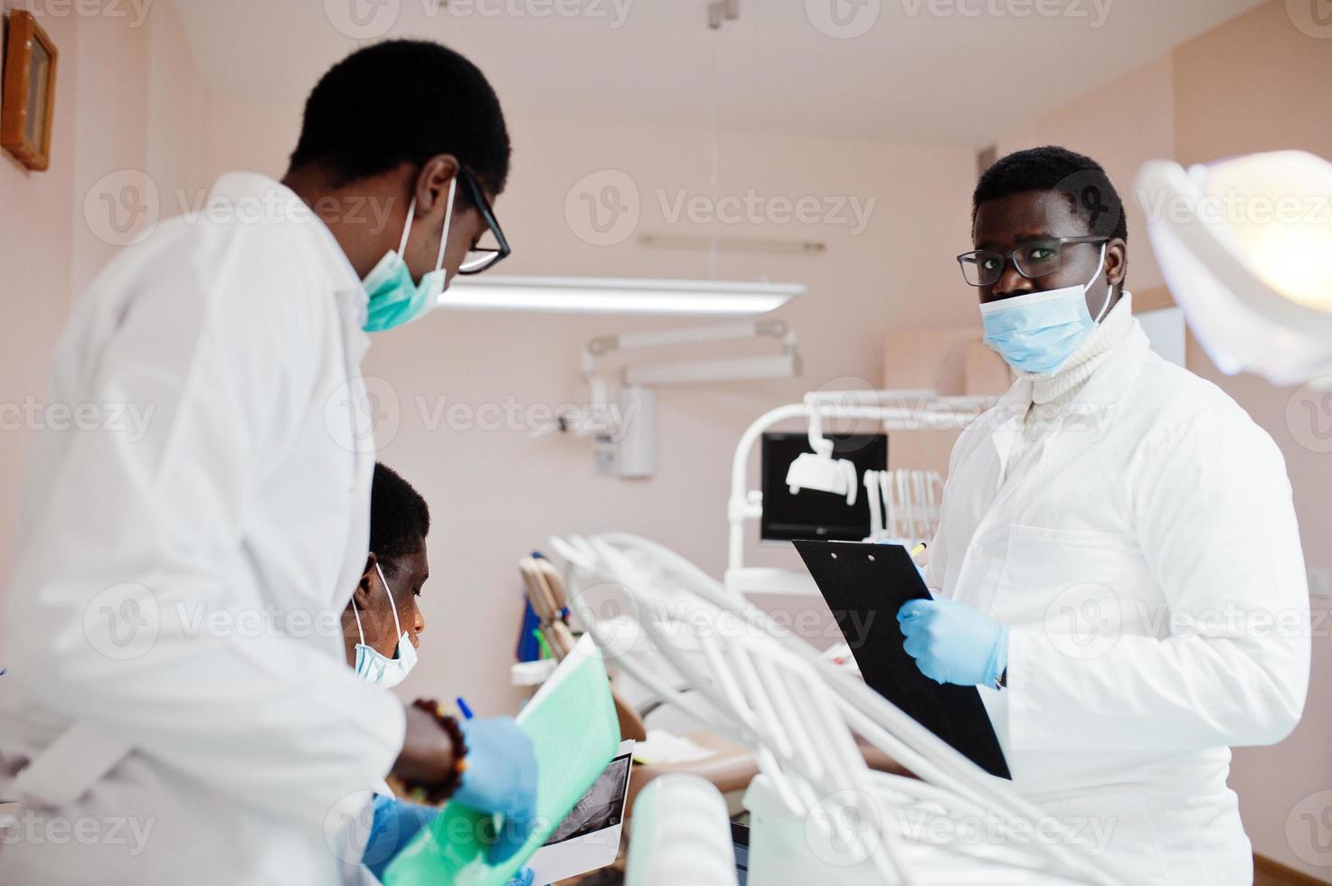 tres médicos afroamericanos trabajando con una laptop, discutiendo con colegas en la clínica dental. foto