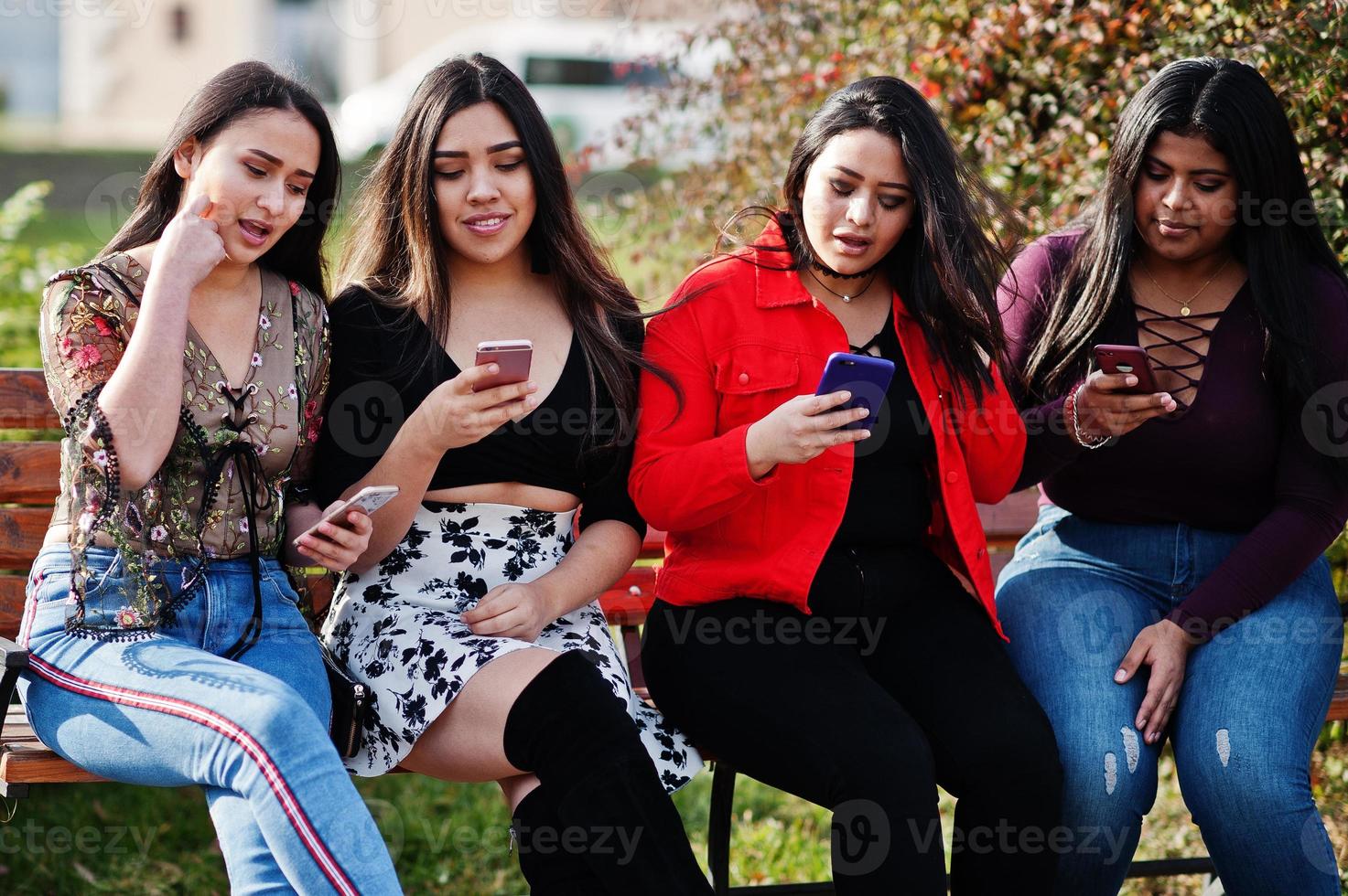 grupo de cuatro chicas latinas felices y bonitas de ecuador posaron en la calle y mirando teléfonos móviles. foto