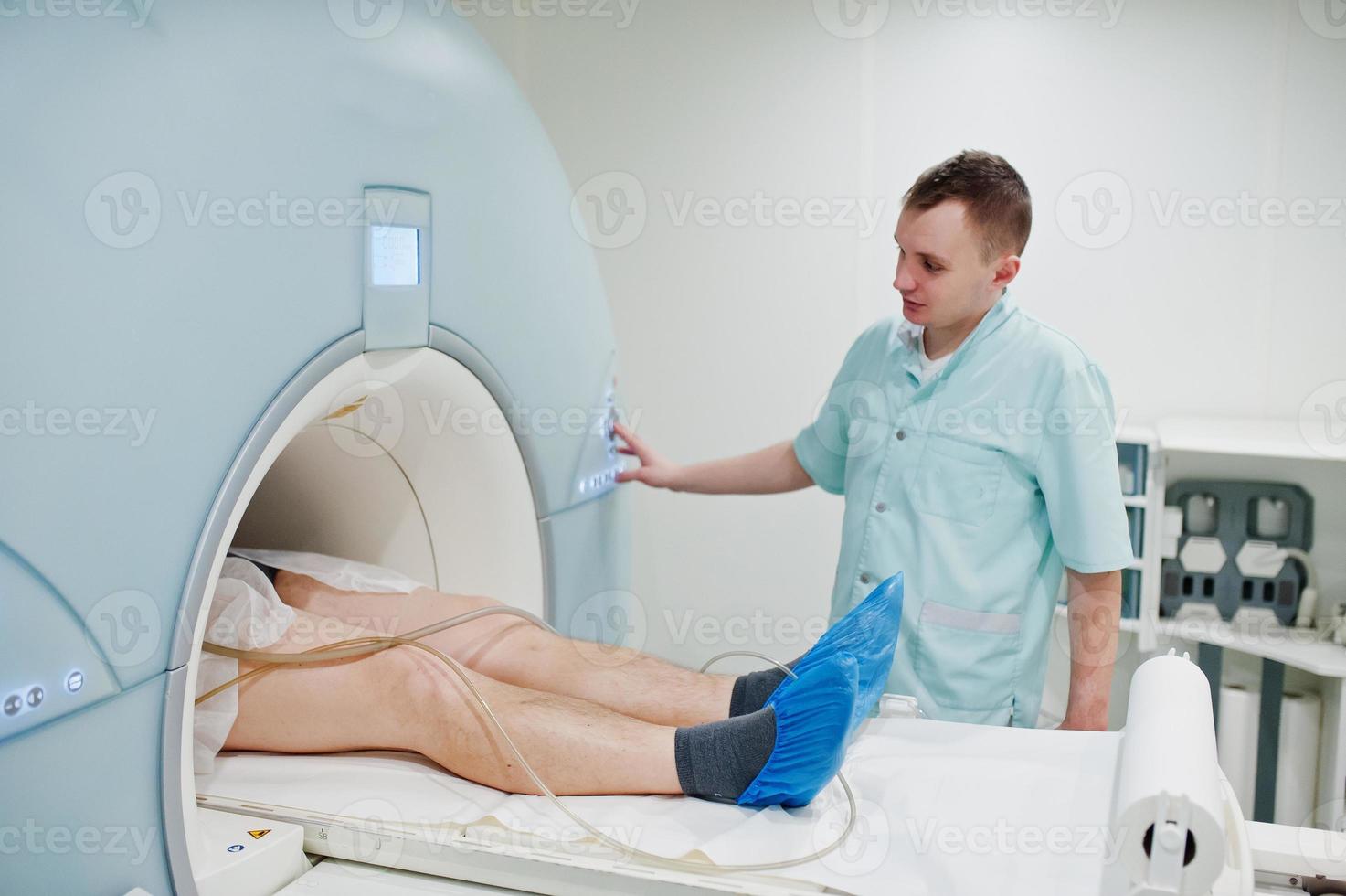 Male doctor turns on magnetic resonance imaging machine with patient inside. photo