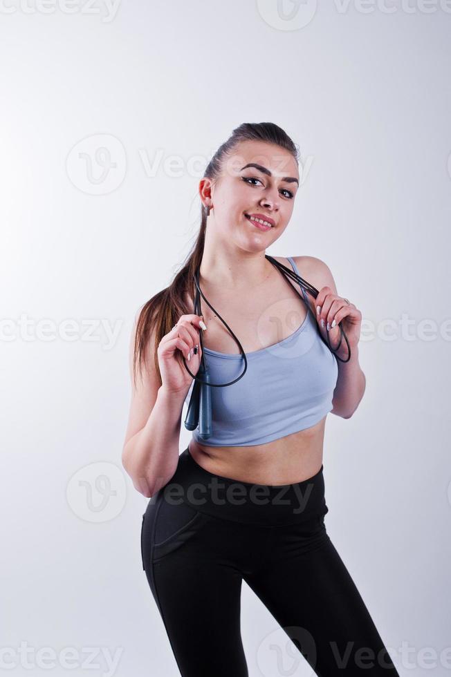 Cheerful attractive young fitness woman in top and black leggings with jump rope isolated over white background. photo