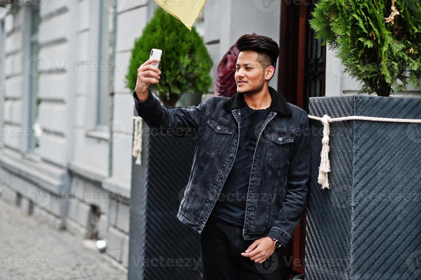 un hombre indio apuesto y de moda con una chaqueta negra de jeans posó al aire libre y se hizo selfie por teléfono. foto