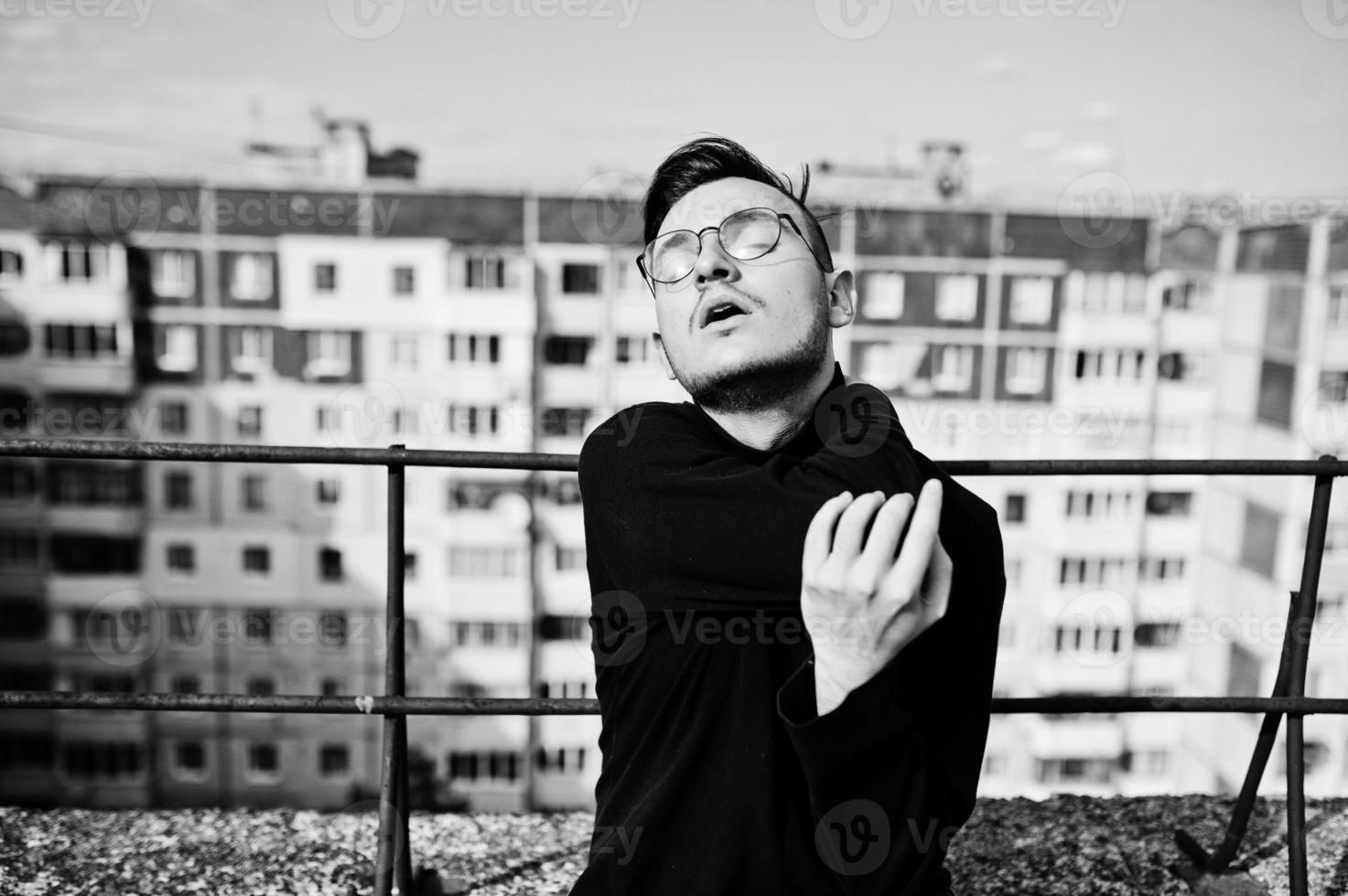 Dreamer stylish macho man in black golf and glasses posed on the roof. photo