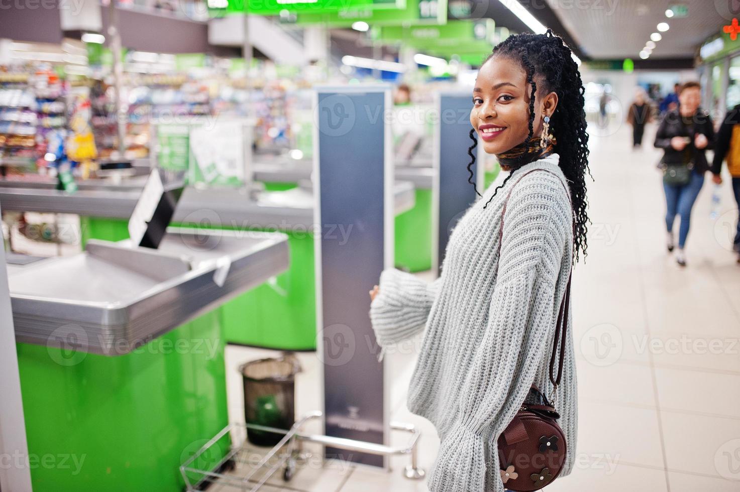 African woman posed in sweater and jeans posed at supermarket against cashier. photo