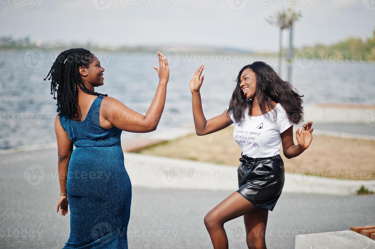 Two african american dark skinned friends female. One of them plus size model, second slim. Having fun and spending time together. Give high five each other. photo