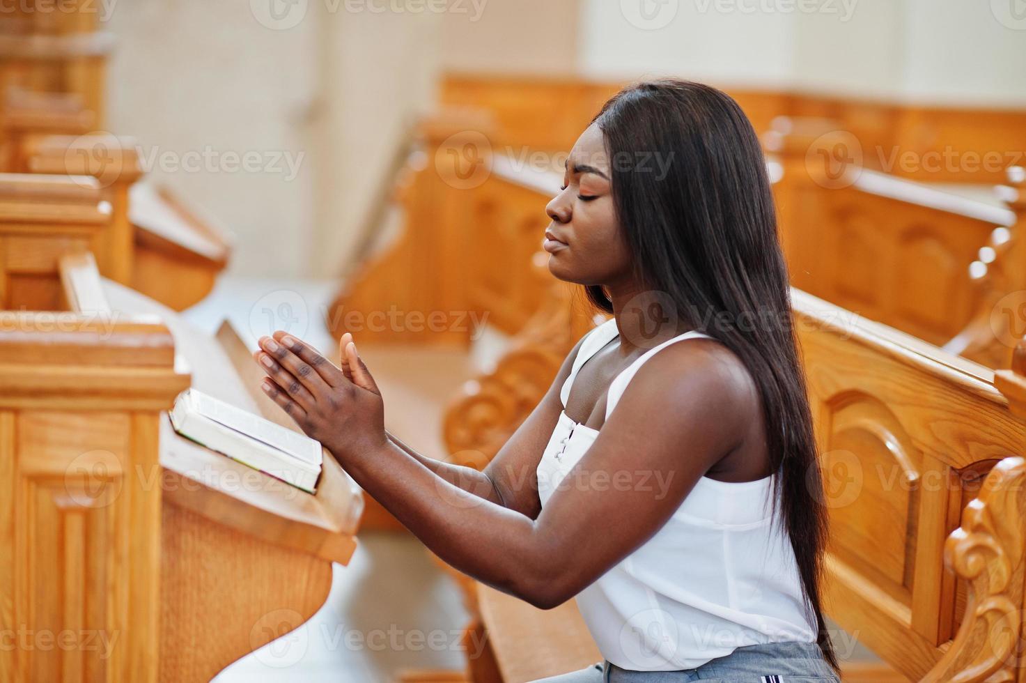 mujer afroamericana rezando en la iglesia. los creyentes meditan en la catedral y tiempo espiritual de oración. chica afro dobló las manos mientras se sentaba en el banco. foto