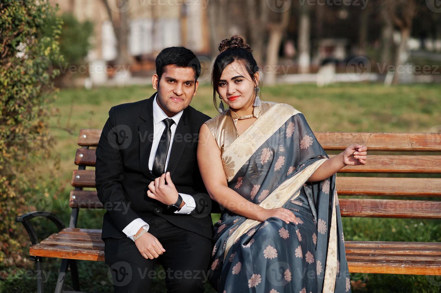 amigos indios elegantes y de moda pareja de mujer en sari y hombre en traje sentado en un banco. foto