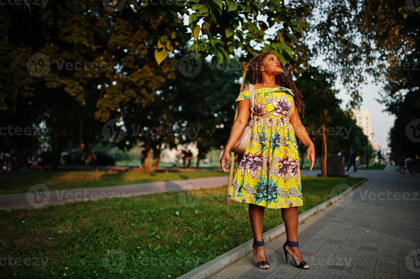Cute small height african american girl with dreadlocks, wear at coloured yellow dress, posed at sunset. photo