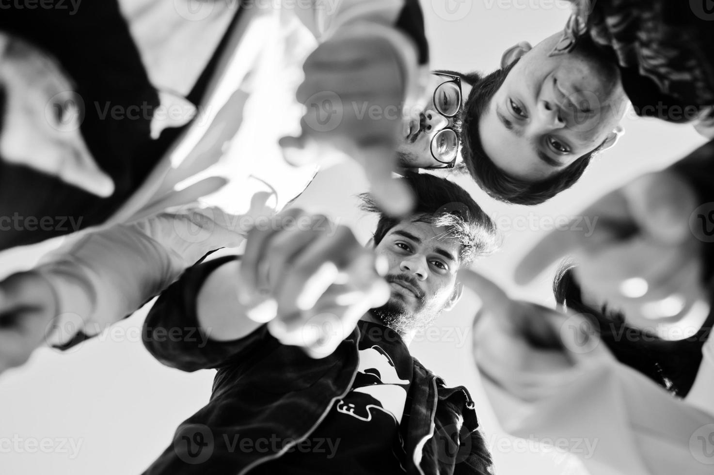 Group of four asian people friends stand on, looking at camera down and show fingers. photo