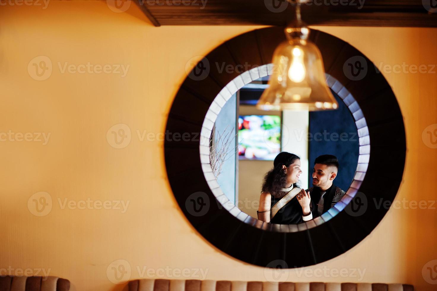 Encantadora pareja india enamorada, vestida con sari y traje elegante, posada en el restaurante en un círculo redondo en la pared. foto